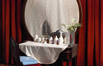 a vanity mirror in front of red curtains with a white table cloth across the front.