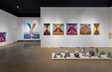 Full view of the gallery containing a selection of volcano, skull-shaped and globe-like ceramics with the background of tufted wool volcano wall hangings