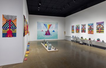 Full view of the gallery containing a selection of volcano, skull-shaped and globe-like ceramics with the background of tufted wool volcano wall hangings