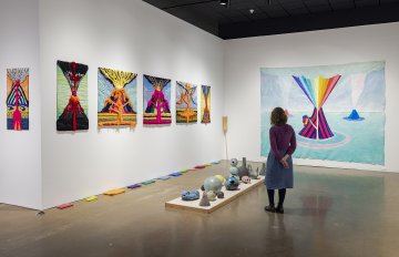 Image of a person standing amongst the multiple wall hangings of volcanoes with ceramic sculptures on the floor