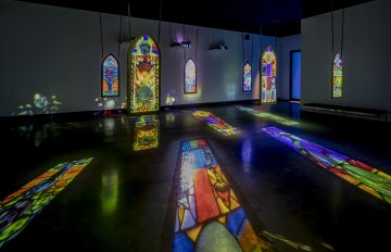 Large stain glass art pieces hung from the ceiling with colourful light reflecting onto the floor