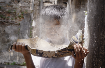 A boy holding onto a hollowed out piece of wood with dust puffing into his face