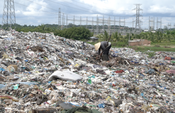 an asian person wearing a straw hat picking through a garbage dump