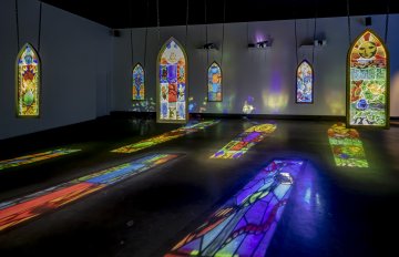 installation shot of various stain glass window pieces hung from the ceiling and colourful light reflecting off the floor