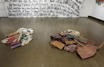 image of gallery exhibition with walls covered in writing and the floor has piles of clothes on it