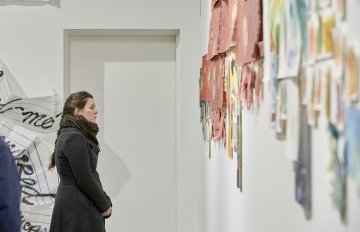 image of gallery exhibition with walls covered in writing with a person admiring the artwork