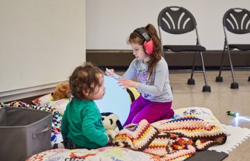 Photo f two toddlers sitting in the sensory room, one of them is wearing noise cancelling headphones