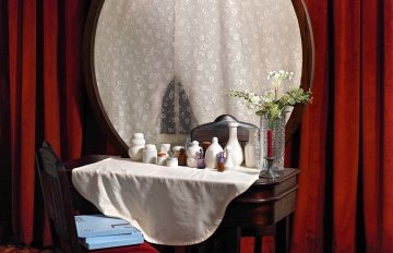 painting of a mirror in front of red curtains hung on the wall and a chair in front of the mirror