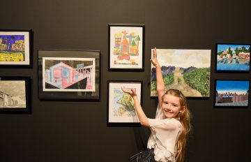 group of artwork hung on wall with young girl pointing towards it