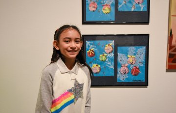 young girl standing in front of artwork hung on the wall