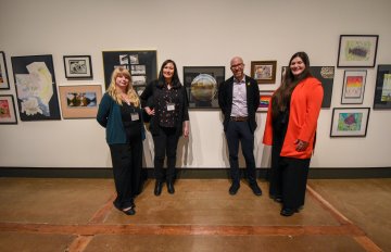 multiple people standing in front of a display of artwork hung on the wall.