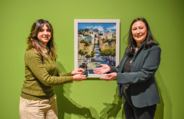 two people standing on either side of an artpiece hung on a green wall