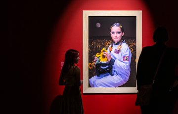 portrait of a girl holding sunflowers hun on a red wall being admired by gallery visitors