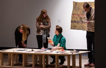 artworks displayed on a table being admired by gallery visitors