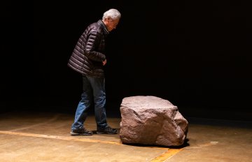 large stone sculpture on floor of gallery being admired by a man