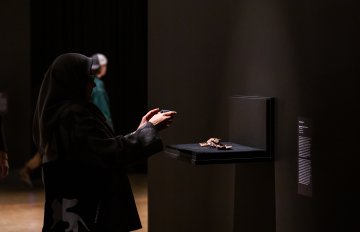 small stone arrtwork hung on wall being admired by gallery visitors