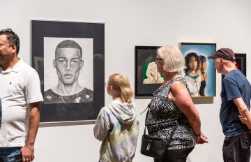 portraits made by students hung on the walls with several people admiring them