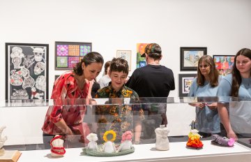 miniature sculptures on display behind glass with several people looking at them