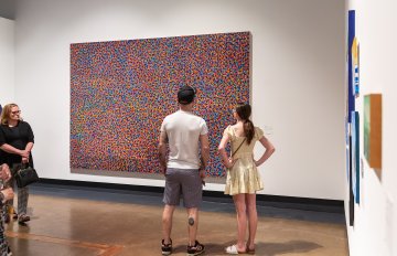 large painting on gallery wall with man and women looking at it