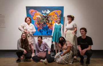 youth council standing in front of their collaborative art piece, a large butterfly painting