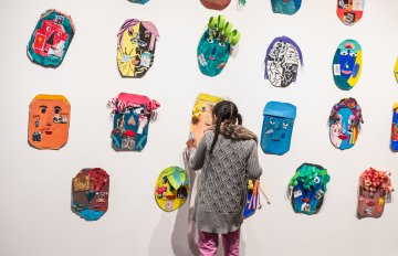 decorative masks hung on the gallery wall with a girl looking at them