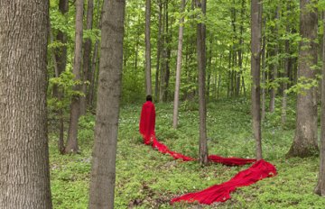 person wearing a long red piece of fabric in the woods with the fabric lining the forest floor