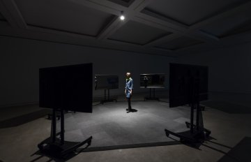 person standing in the middle of a circular display of tv screens