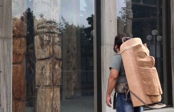 man looking in a shop window with a part of a totem pole strapped to his back