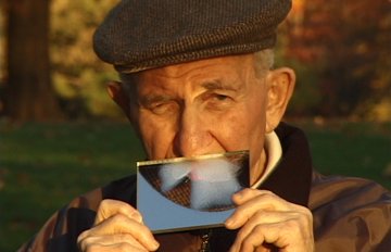 photograph of an elderly man holding a piece of paper over his mouth