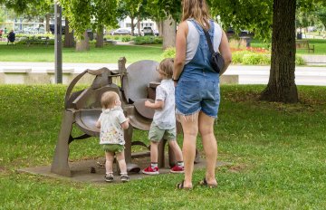 Person with two young childen standing in front of a metal sculpture