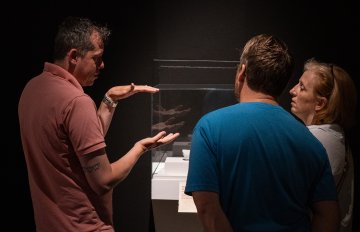 Group of people surrounding a glass enclosure in the dimly lit gallery