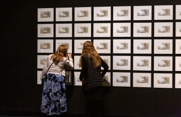 many pictures hung on a black wall looked at by two women