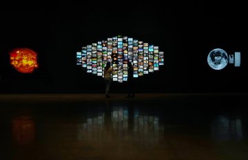 Two people standing in front of a digital video installation with 60 different videos