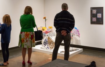 The backs of three people as they gaze at artwork on the floor and walls in front of them