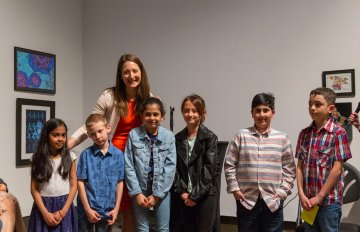 Group of school students standing with a teacher in front of artwork displayed in the Expressions exhibition