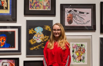 Young person standing in fromt of a white wall filled with student artwork