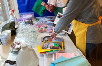Two adults standing beside a craft table preparing art materials