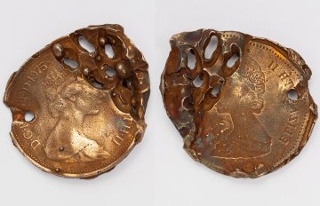Photograph of two altered pennies with drill holes running through them. They are on a white background.