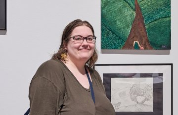 Young person standing next to their artwork smiling into the camera