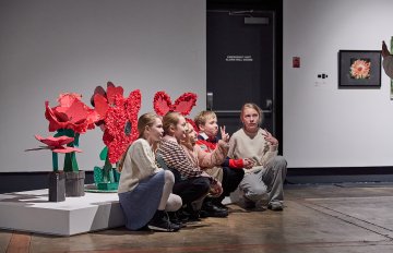 Group of four kids sitting on the floor next to their sculptural installation of poppies