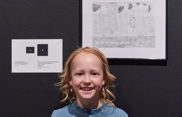 Young person standing next to their artwork smiling into the camera