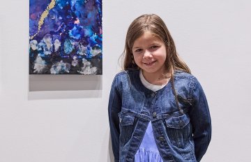 Young person standing next to their artwork smiling into the camera