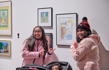 Two smiling individuals pose alongside their artwork