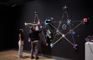 Two individuals standing in front of a black wall with star and constellation shapes