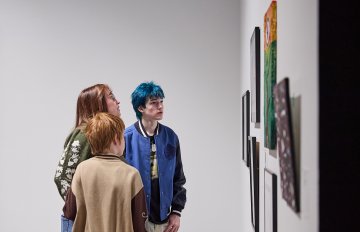 A group of three people gazing at a selection of artworks on a white wall