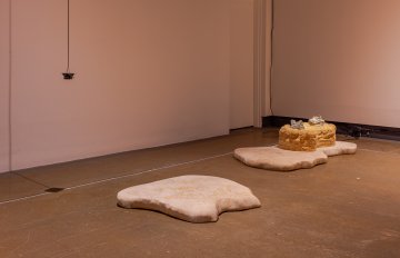 Installation view featuring two sculptures on the floor and 1 hanging wire. 