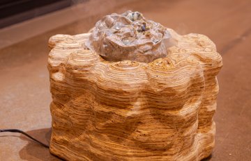 A sculpture sitting on the ground emitting a scent.