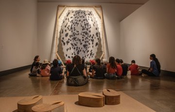 Group of campers sitting on the Gallery floor in front of a large fur animal skin