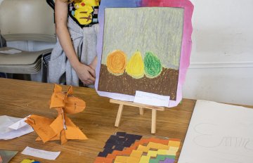 Camper standing behind an easel displaying a collection of artwork
