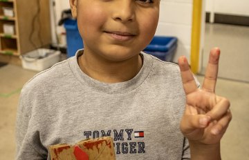Camper holding a print template smiling and doing a peace sign with their hands